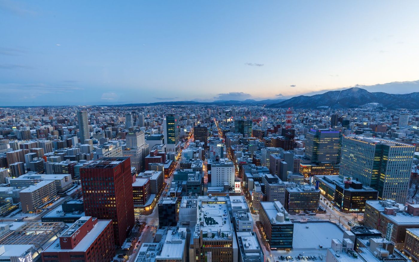 Sapporo's snow-covered city blocks at dusk, mountains on the horizon