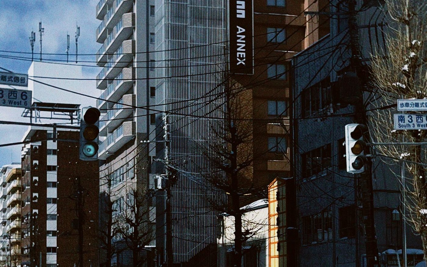 A snow-covered Sapporo street with tall buildings and overhead wires on a bright winter day