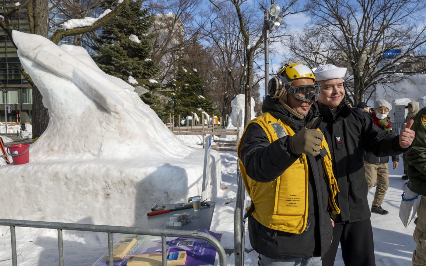 A large carved snow sculpture in a snowy park with its building crew standing in front of it