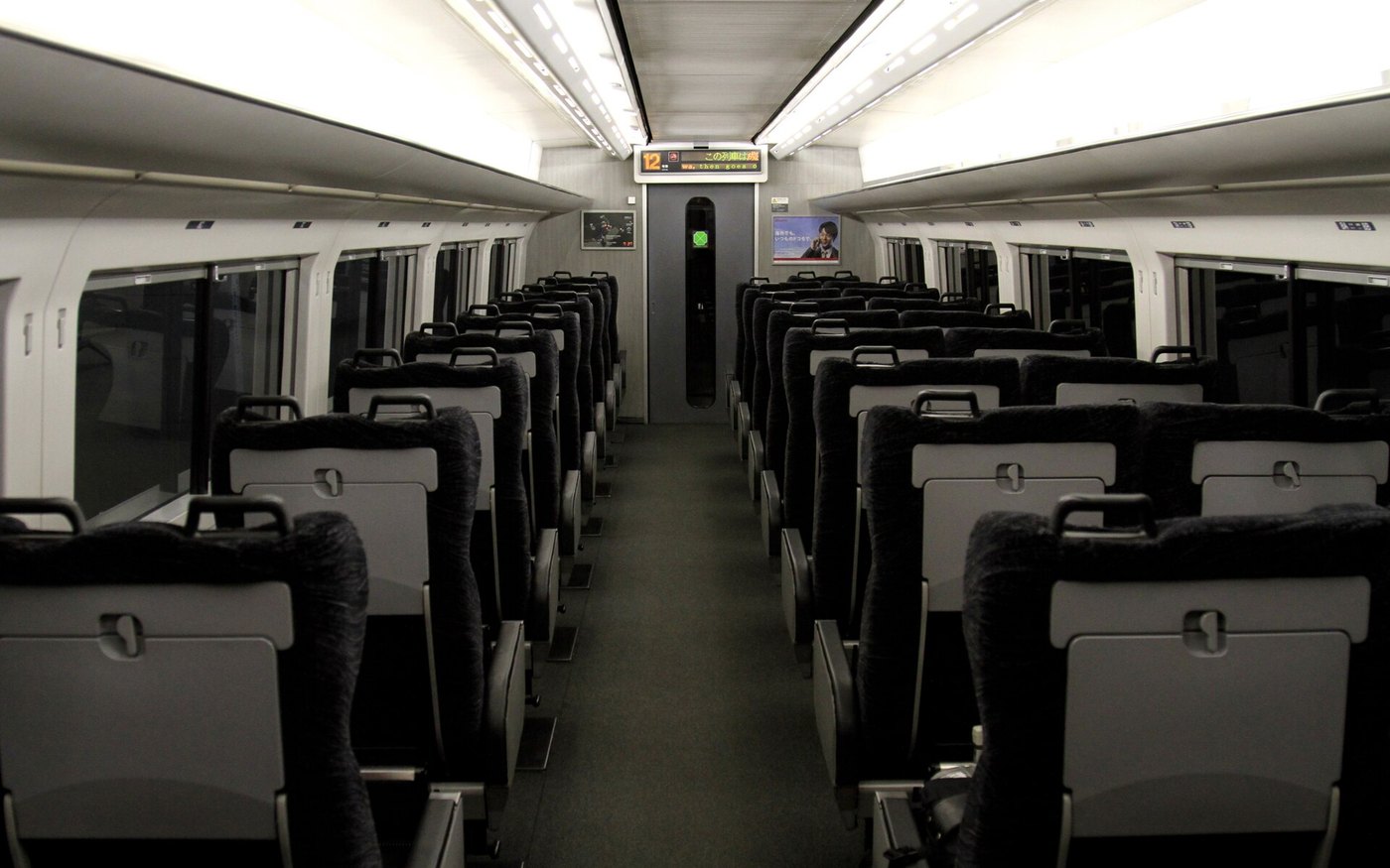 The dark seat rows and grey aisle of a Narita Express car, photographed from one end of the coach