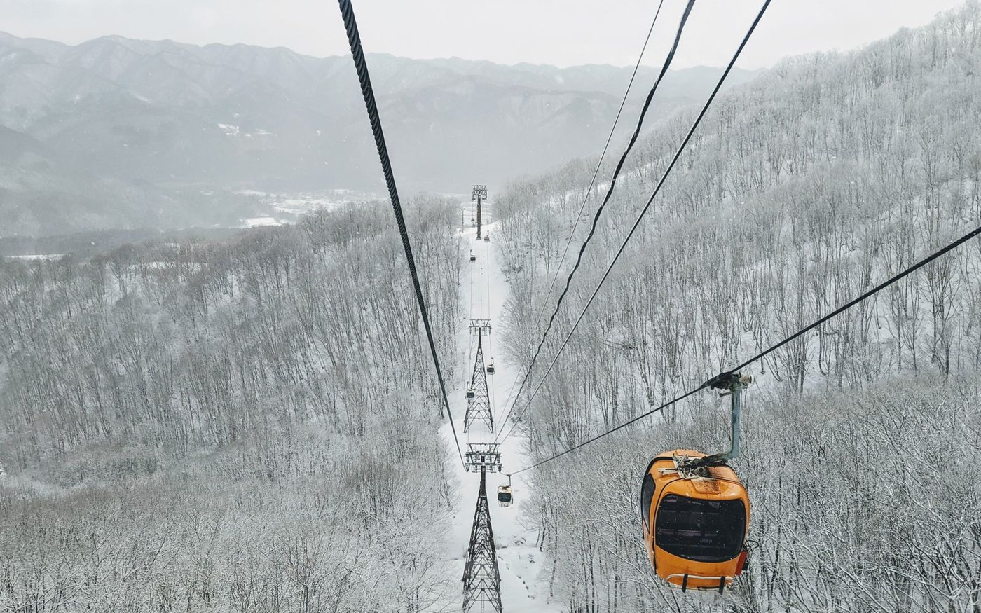 An orange cable car above a snow-covered forested valley