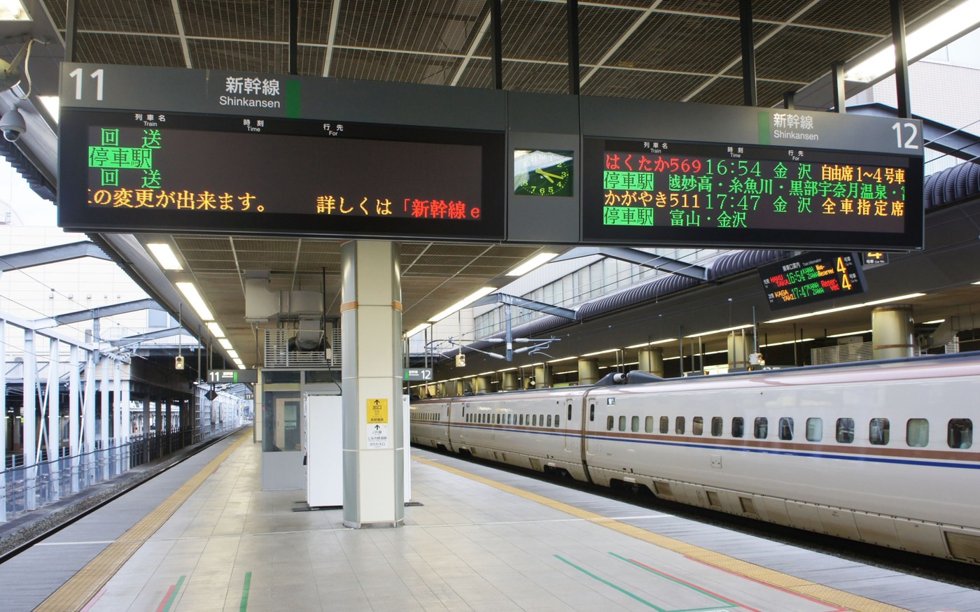 A shinkansen platform at Nagano station with a train drawn up and an overhead departure display