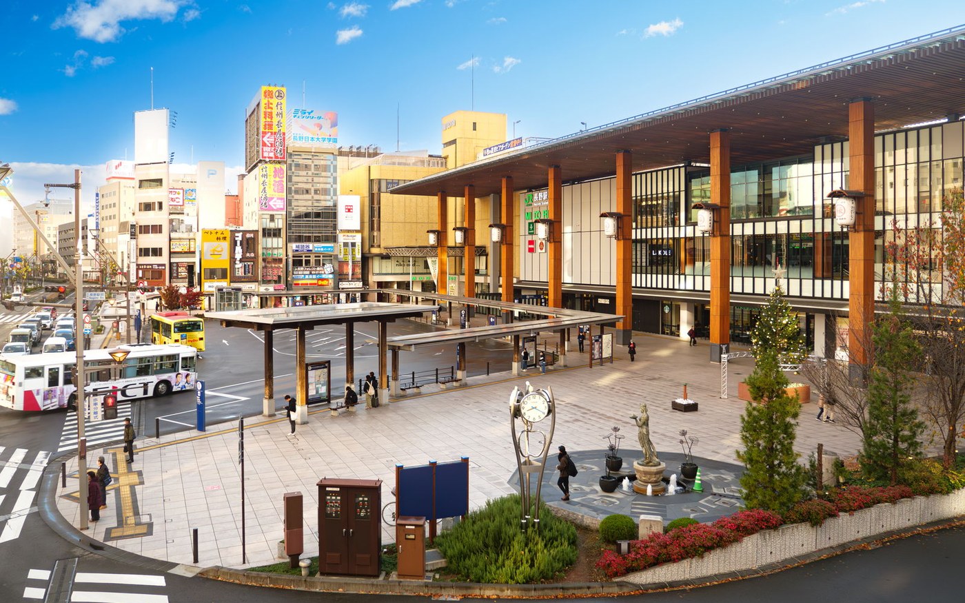 The glass frontage of Nagano station with a bus turning in front of it