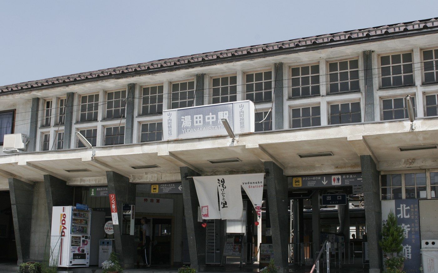 The low wooden building of Yudanaka station on the Nagano Dentetsu line, with a train at the platform