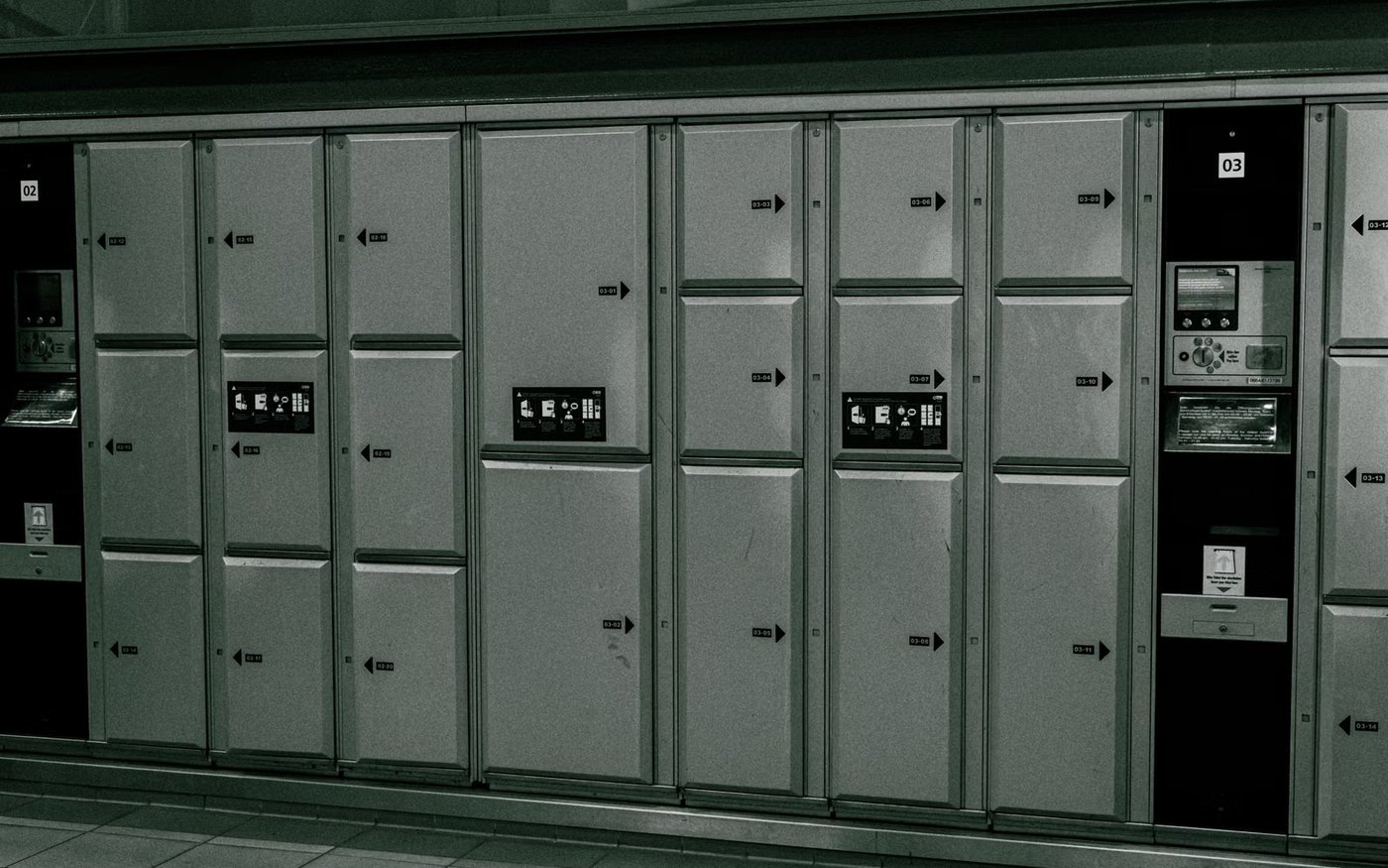 A bank of coin lockers at a Japanese station with the size chart printed on the doors