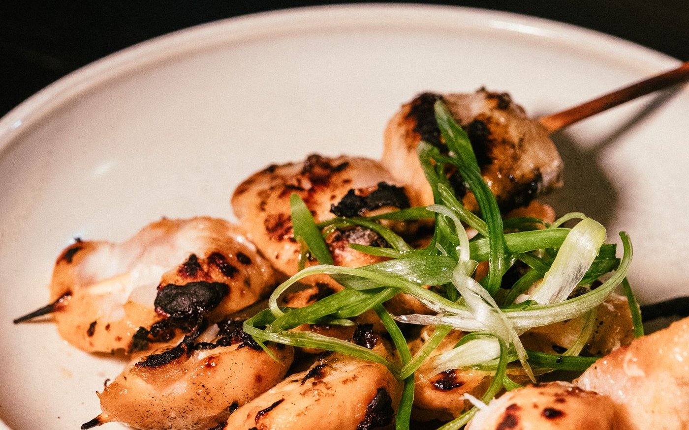 Grilled chicken skewers with sliced green leek on a cream ceramic plate