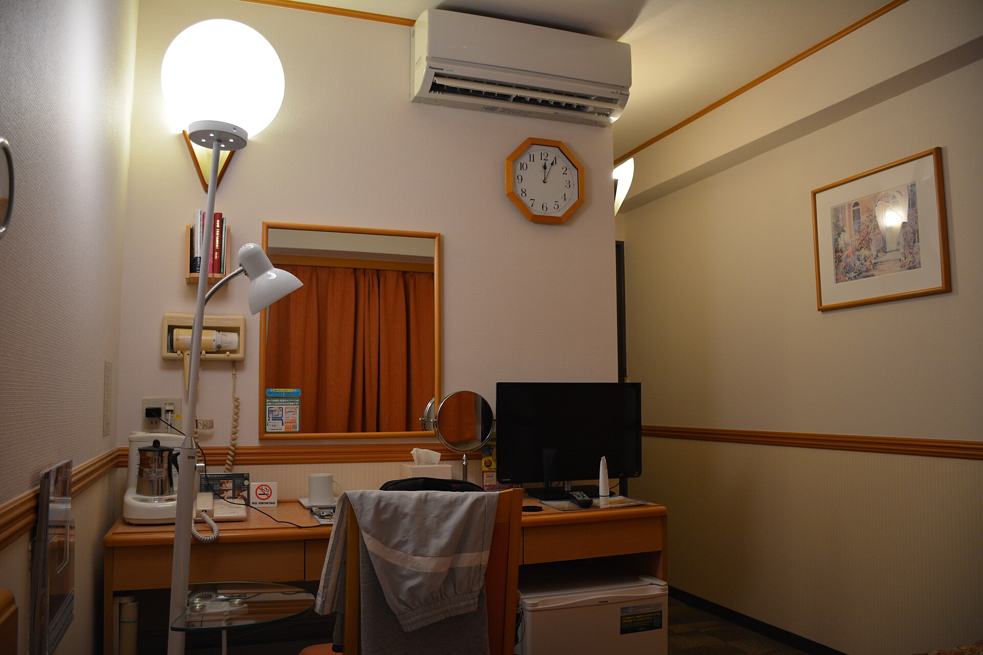 A compact Japanese business-hotel room: desk, kettle, TV and mini-fridge