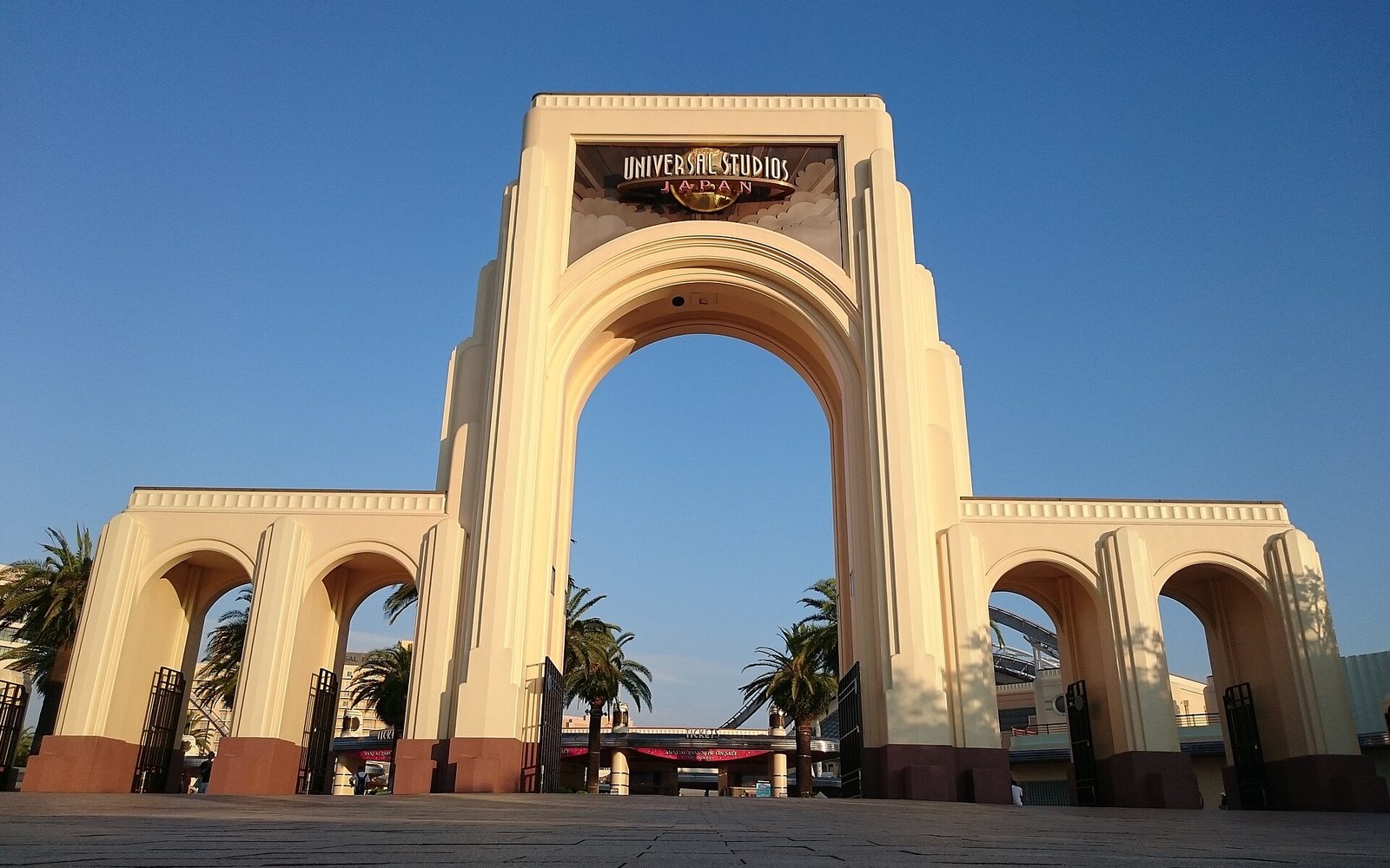 The Universal Studios Japan entrance portal from the empty forecourt, the park name and globe logo on the central arch