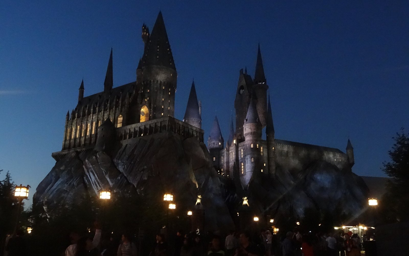 Hogwarts Castle lit from within at night, with lanterns along the path and a crowd below