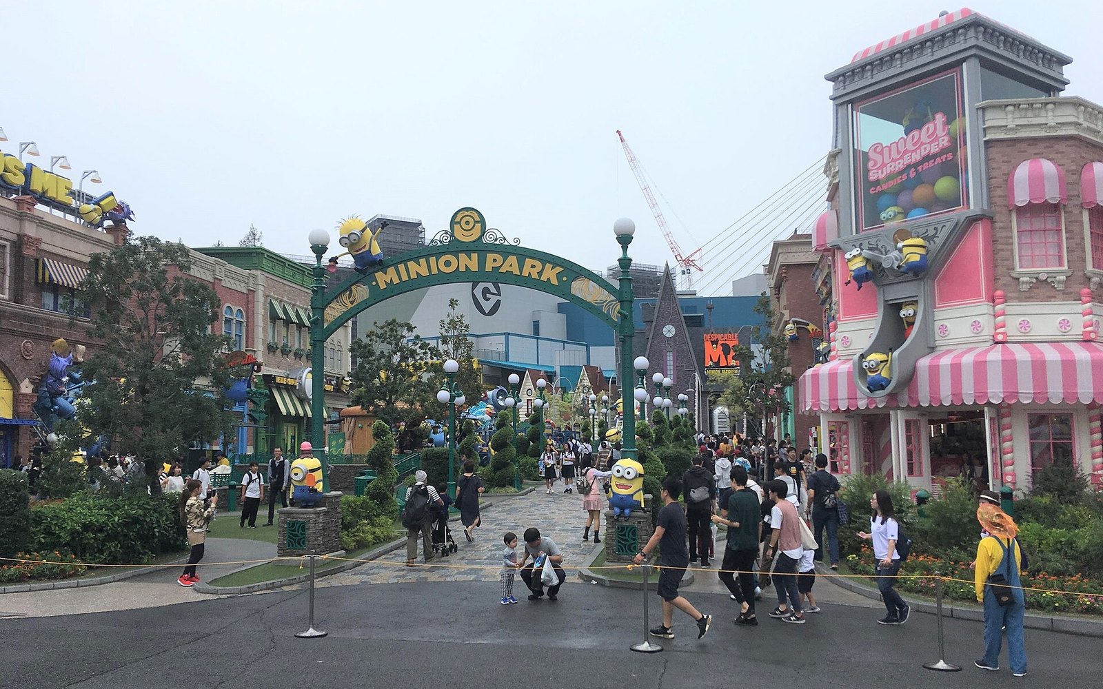 The green Minion Park entrance arch with Minion figures on the buildings and visitors walking through