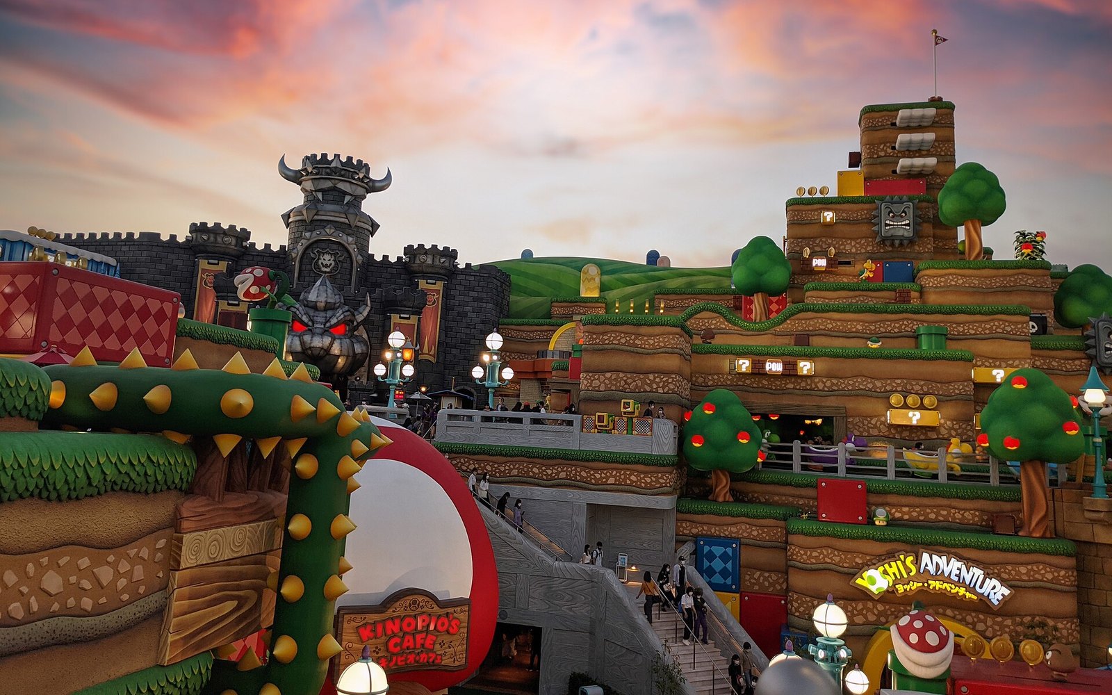 Super Nintendo World at dusk with lit lanterns, glowing question blocks and visitors moving between levels