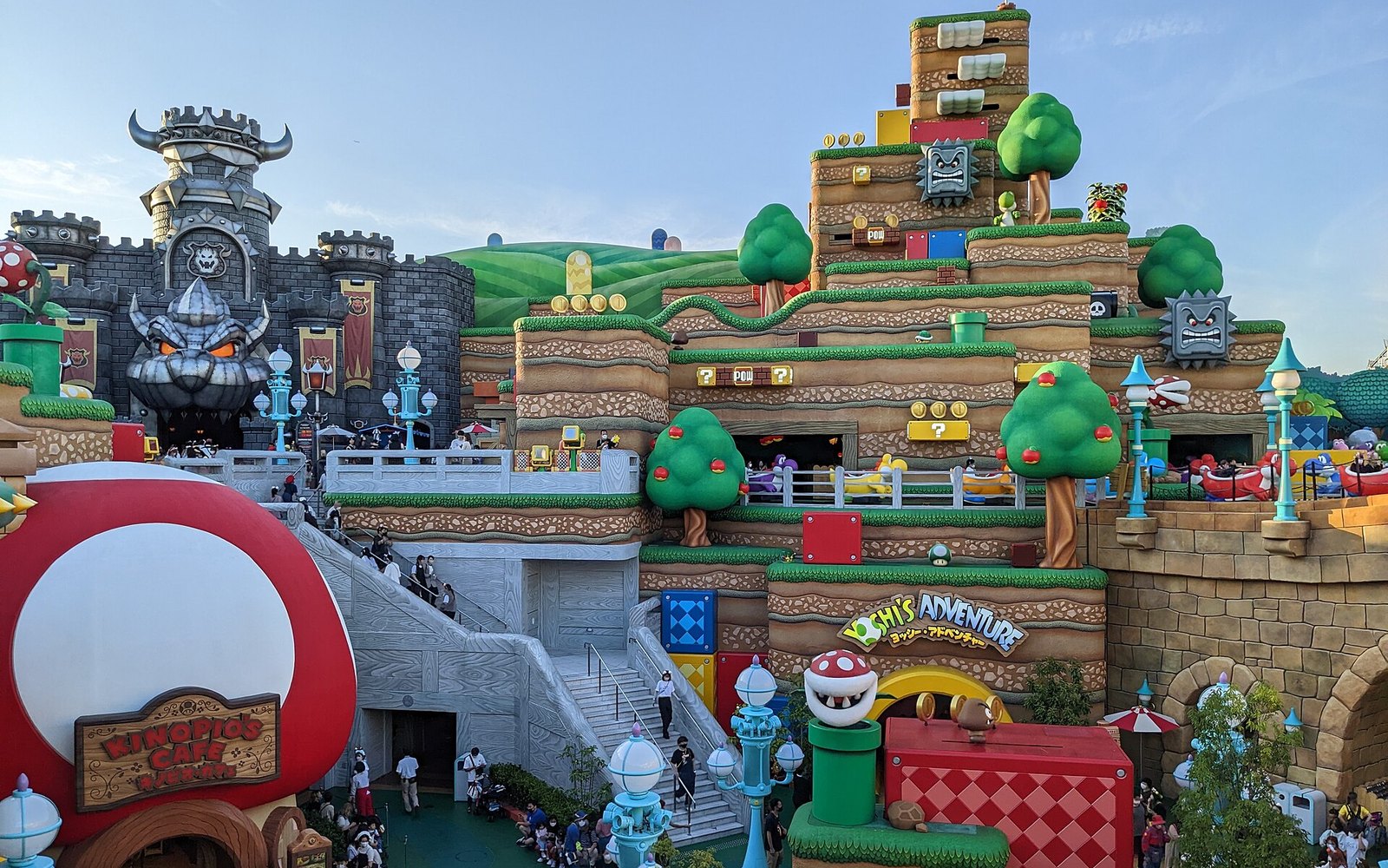 The Mushroom Kingdom at Super Nintendo World with Bowser's Castle, tiered blocks and Yoshi's Adventure, crowded with visitors