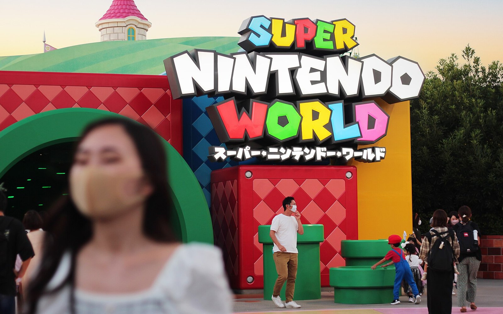 The Super Nintendo World entrance sign above a green pipe portal, with visitors walking through