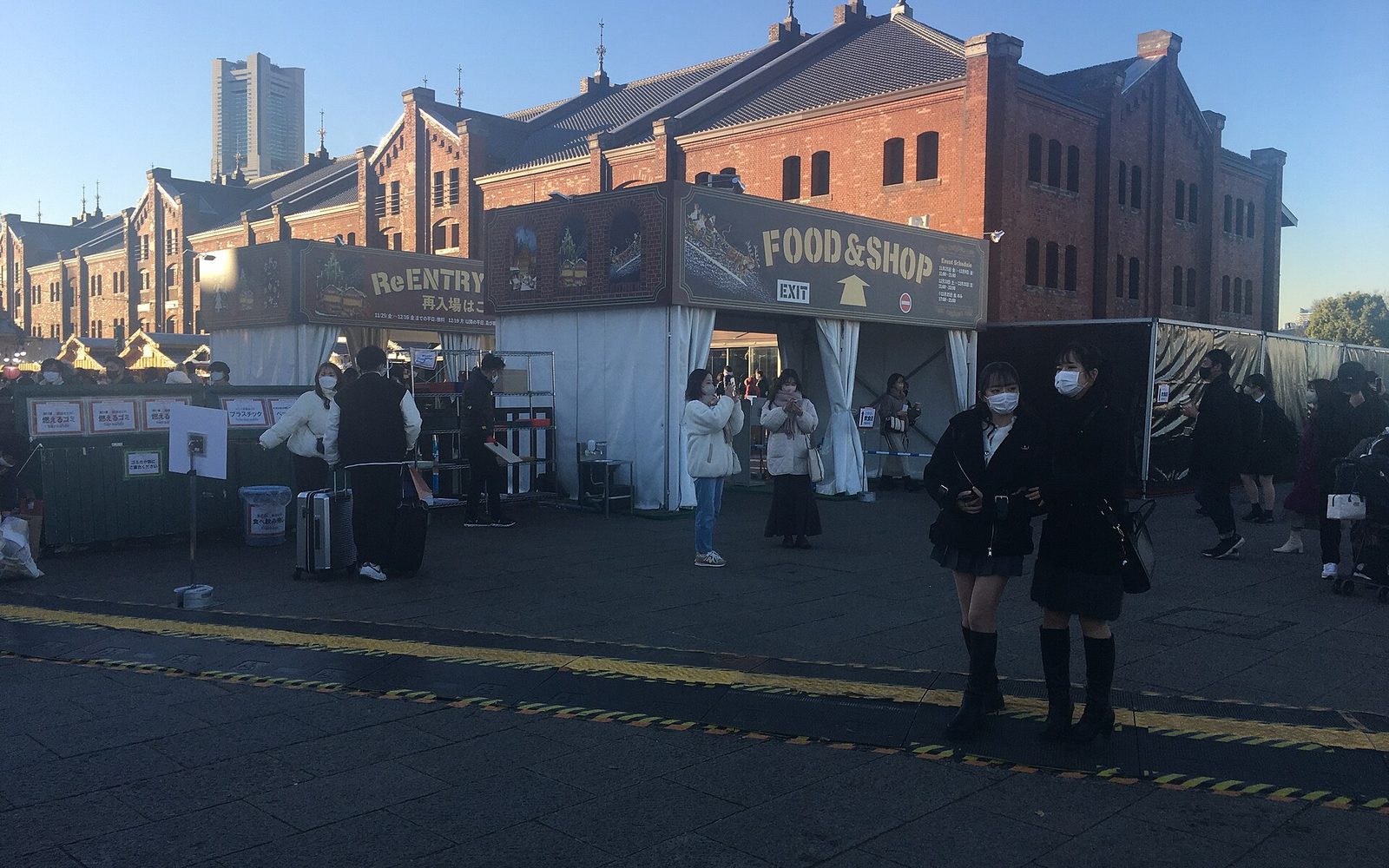 White gateway tents marked FOOD and SHOP beside a red brick warehouse, with visitors walking past